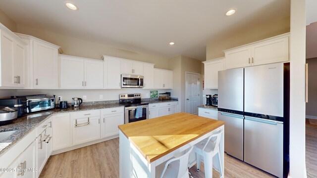 kitchen with white cabinets, light wood-style floors, appliances with stainless steel finishes, and light stone counters