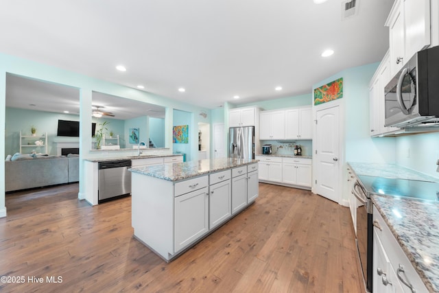 kitchen with sink, appliances with stainless steel finishes, white cabinetry, light stone countertops, and a kitchen island