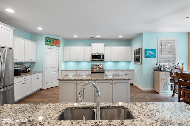 kitchen featuring light stone counters, stainless steel appliances, sink, and a center island with sink