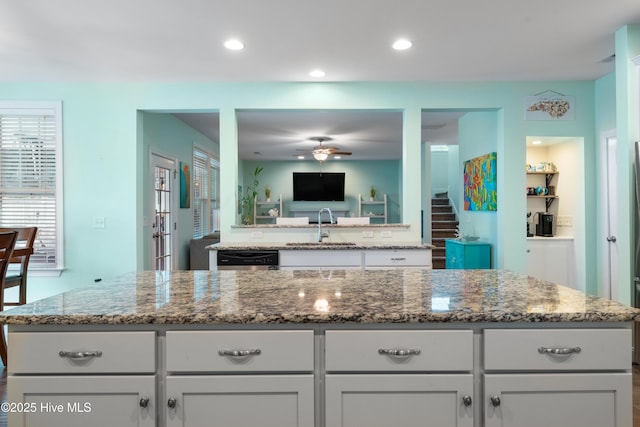 kitchen featuring sink, stainless steel dishwasher, dark stone counters, and a kitchen island