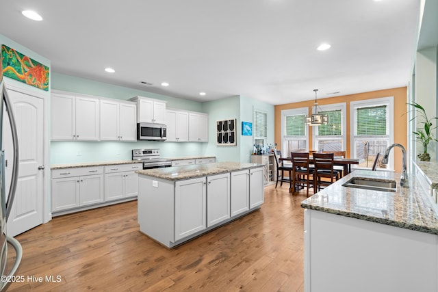 kitchen featuring an island with sink, sink, white cabinets, hanging light fixtures, and stainless steel appliances