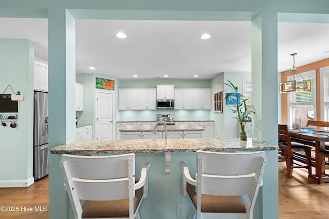 kitchen with hanging light fixtures, a breakfast bar area, white cabinets, and appliances with stainless steel finishes