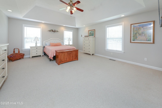 carpeted bedroom with multiple windows, ceiling fan, and a tray ceiling