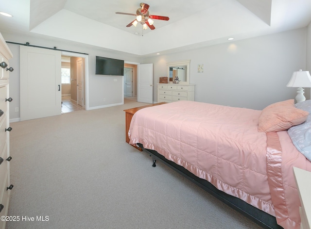 carpeted bedroom with a barn door and a tray ceiling