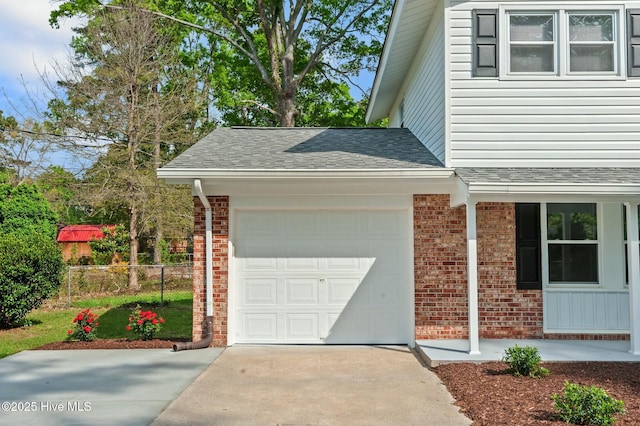 view of side of property with concrete driveway, an attached garage, brick siding, fence, and a shingled roof