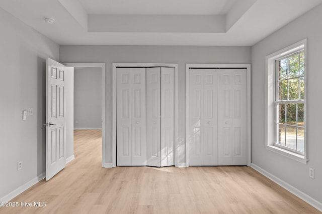 unfurnished bedroom featuring multiple windows, multiple closets, and light wood-type flooring