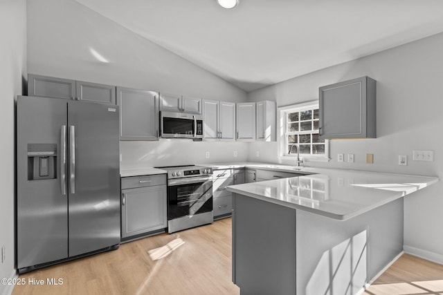 kitchen featuring sink, gray cabinets, appliances with stainless steel finishes, vaulted ceiling, and kitchen peninsula