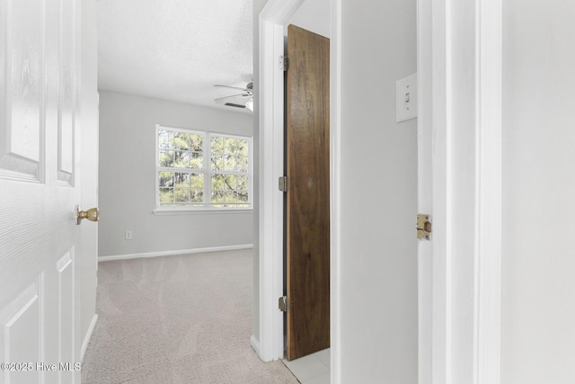 hallway with light colored carpet and a textured ceiling