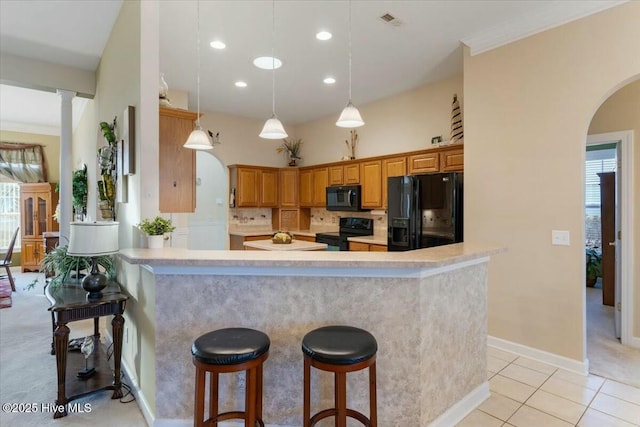 kitchen featuring pendant lighting, light tile patterned floors, a breakfast bar, backsplash, and black appliances