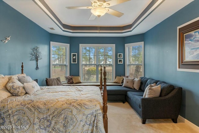 bedroom featuring ceiling fan, a raised ceiling, and light carpet