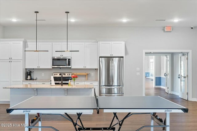 kitchen with decorative light fixtures, white cabinetry, a kitchen island with sink, light stone counters, and stainless steel appliances