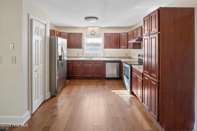 kitchen with sink, hardwood / wood-style flooring, stainless steel appliances, light stone countertops, and a textured ceiling