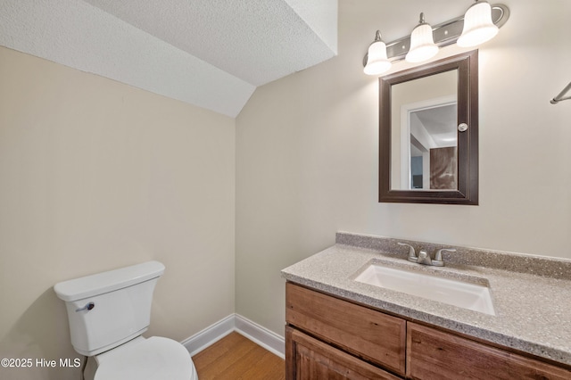 bathroom with lofted ceiling, hardwood / wood-style flooring, vanity, a textured ceiling, and toilet