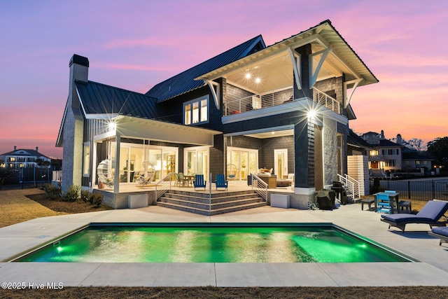 back house at dusk featuring a fenced in pool, a patio area, and a balcony