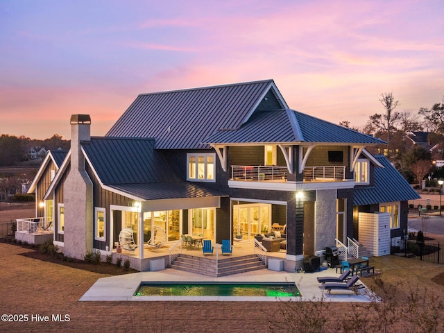 back house at dusk with an outdoor living space, a patio area, and a balcony