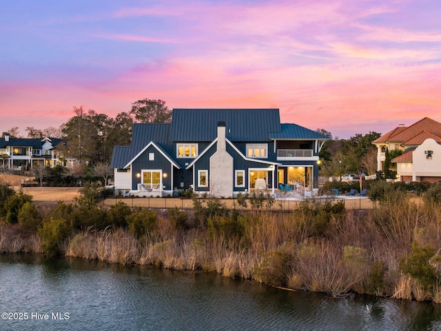 back house at dusk featuring a balcony and a water view