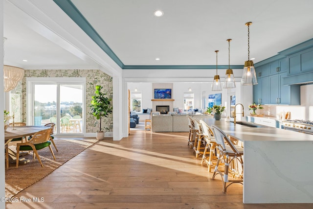 kitchen featuring decorative light fixtures, blue cabinets, sink, ornamental molding, and light wood-type flooring