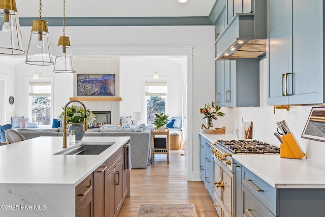 kitchen with sink, high end stove, an island with sink, decorative light fixtures, and custom exhaust hood