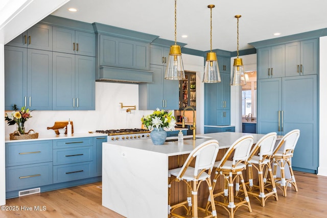 kitchen with a kitchen island with sink, hanging light fixtures, light hardwood / wood-style floors, and blue cabinetry