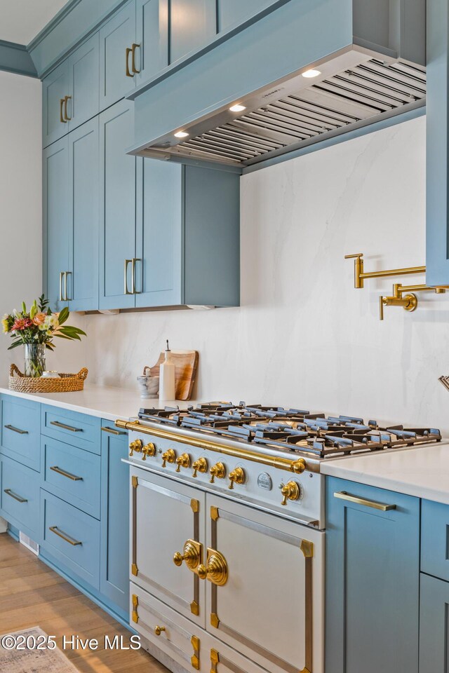 kitchen featuring ventilation hood, blue cabinets, backsplash, and light hardwood / wood-style flooring