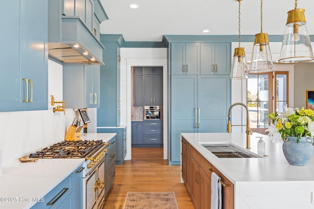 kitchen with appliances with stainless steel finishes, sink, hanging light fixtures, custom exhaust hood, and light hardwood / wood-style floors