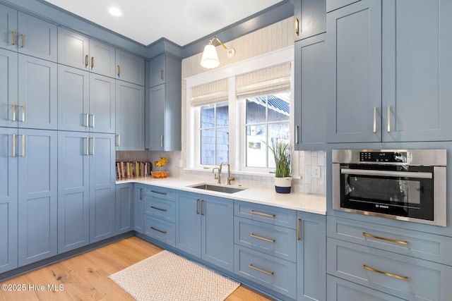 kitchen with blue cabinets, sink, decorative backsplash, stainless steel oven, and light wood-type flooring