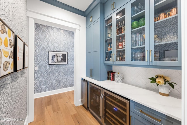 bar with wine cooler, blue cabinetry, light stone counters, light hardwood / wood-style flooring, and backsplash