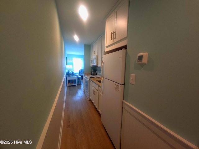 kitchen with white cabinetry, white appliances, and light hardwood / wood-style floors