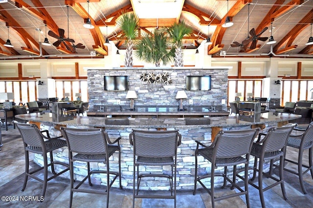 kitchen featuring beam ceiling, high vaulted ceiling, dark stone countertops, and a kitchen bar