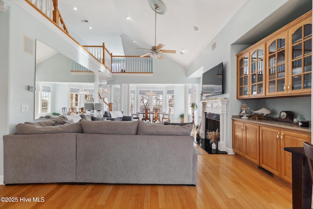 living room featuring ornamental molding, a premium fireplace, ceiling fan with notable chandelier, and light wood-type flooring