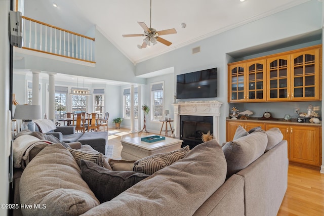 living room featuring crown molding, high vaulted ceiling, light wood-type flooring, ceiling fan, and decorative columns