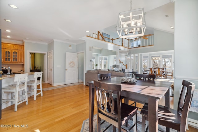 dining area with a towering ceiling, ornamental molding, light wood-type flooring, and a notable chandelier