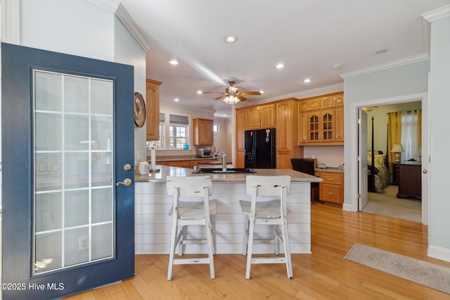 kitchen with sink, light hardwood / wood-style flooring, a kitchen breakfast bar, black fridge with ice dispenser, and kitchen peninsula