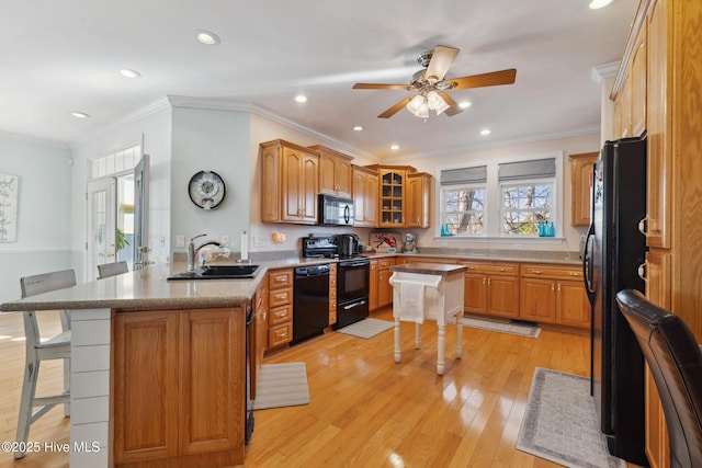 kitchen featuring a breakfast bar, black appliances, sink, kitchen peninsula, and light wood-type flooring