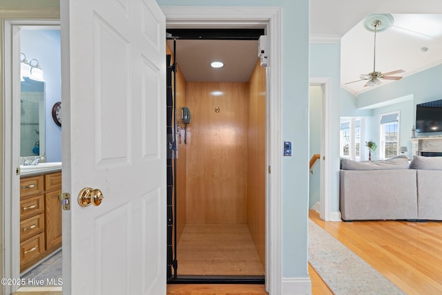 interior space featuring crown molding, ceiling fan, vanity, wood-type flooring, and elevator