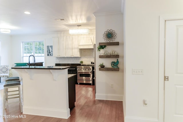 kitchen featuring a breakfast bar, stainless steel stove, sink, decorative backsplash, and light hardwood / wood-style flooring