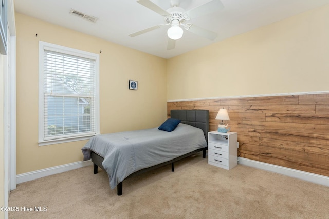 carpeted bedroom featuring multiple windows, wooden walls, and ceiling fan