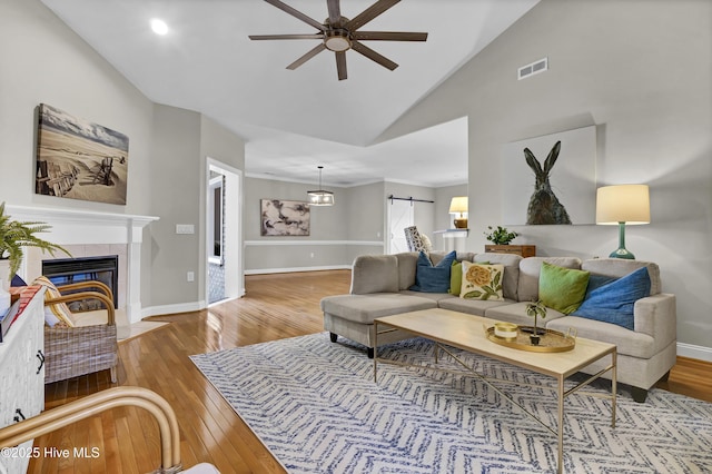 living room with hardwood / wood-style floors, high vaulted ceiling, a fireplace, ceiling fan, and a barn door