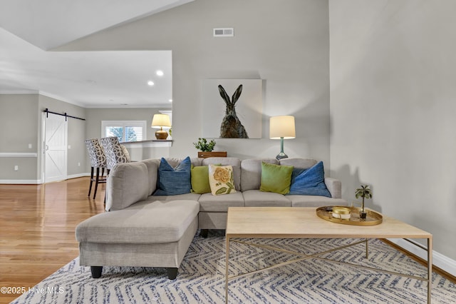 living room with vaulted ceiling, wood-type flooring, a barn door, and ornamental molding