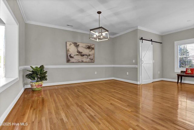 empty room featuring crown molding, wood-type flooring, a barn door, and a chandelier