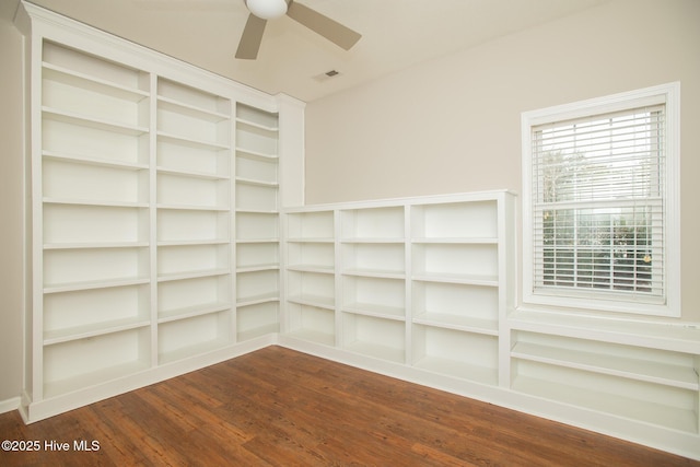 empty room with built in shelves, ceiling fan, and dark hardwood / wood-style flooring