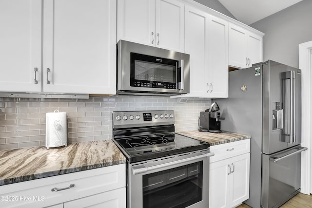 kitchen featuring appliances with stainless steel finishes, backsplash, white cabinets, vaulted ceiling, and dark stone counters