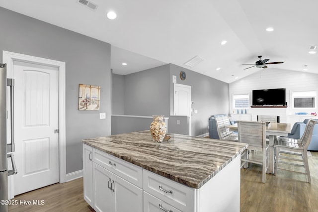 kitchen featuring white cabinetry, lofted ceiling, a center island, light stone counters, and light hardwood / wood-style floors