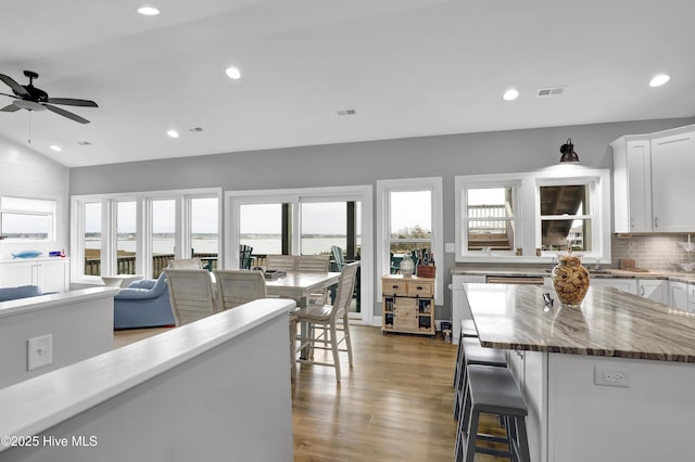 kitchen with lofted ceiling, a breakfast bar area, tasteful backsplash, hardwood / wood-style flooring, and white cabinets