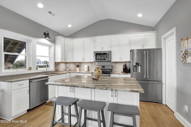 kitchen with sink, white cabinetry, stainless steel appliances, light stone counters, and a kitchen island