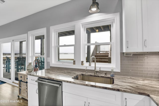 kitchen featuring tasteful backsplash, white cabinetry, dishwasher, sink, and dark stone counters