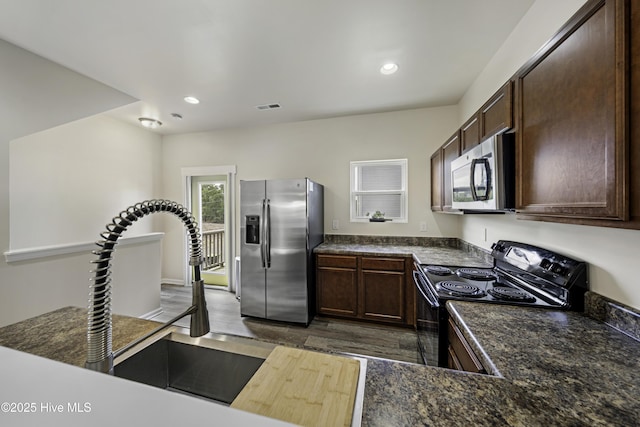 kitchen with stainless steel appliances, dark brown cabinets, dark stone countertops, and dark hardwood / wood-style flooring