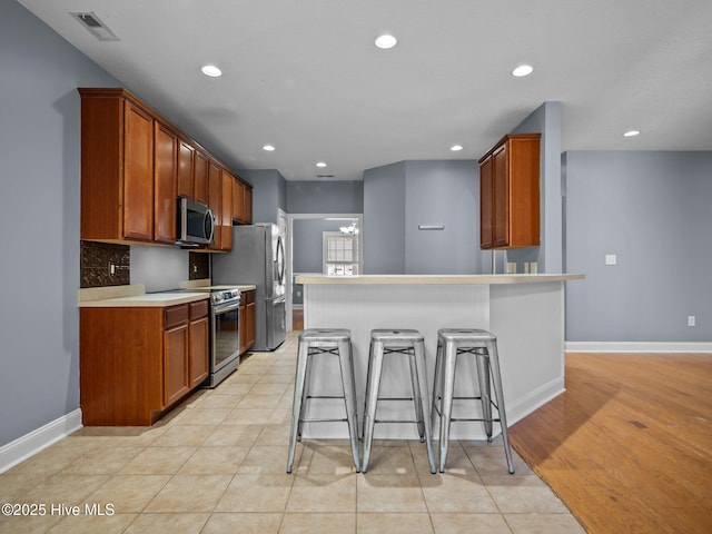 kitchen featuring light tile patterned flooring, appliances with stainless steel finishes, backsplash, and a kitchen breakfast bar