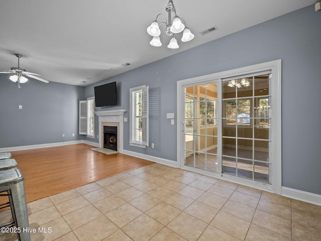 unfurnished living room with light tile patterned flooring and ceiling fan with notable chandelier