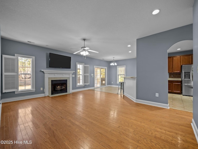 unfurnished living room featuring ceiling fan with notable chandelier, a healthy amount of sunlight, a tile fireplace, and light hardwood / wood-style flooring